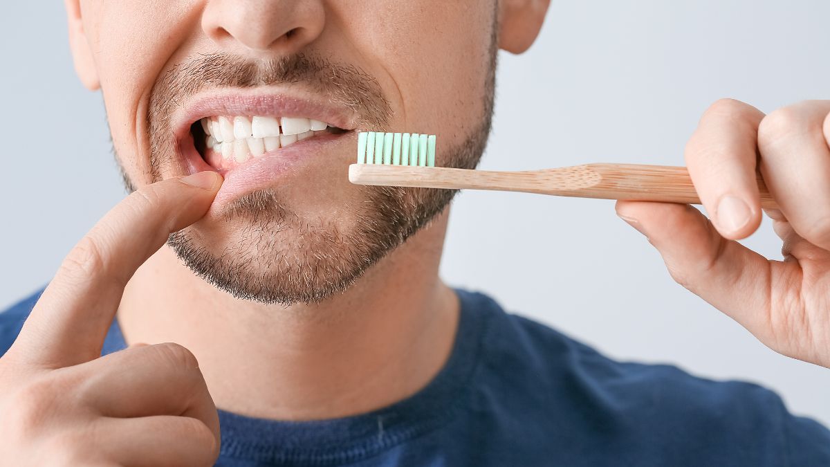 Man Pointing To His Gums While Holding A Toothbrush
